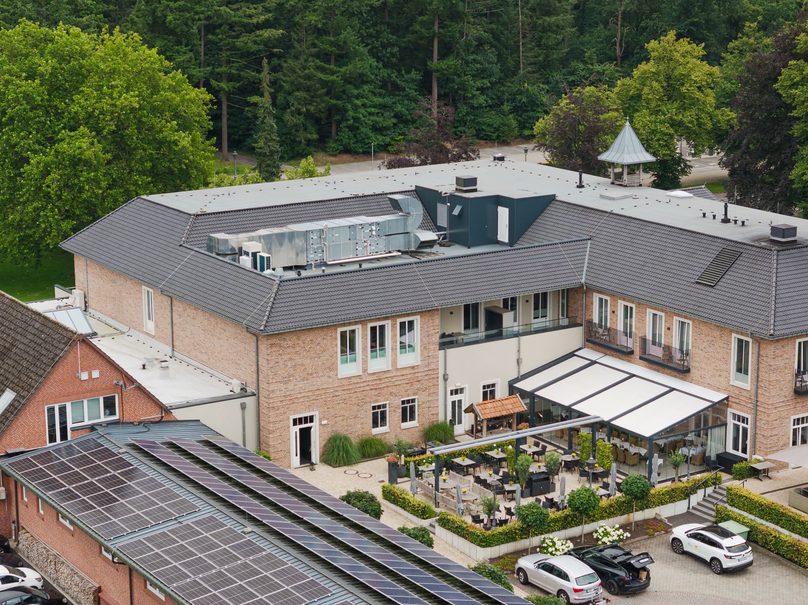 Haupthaus aus Klinker mit Terrasse und Markisen, davor Parkplätze